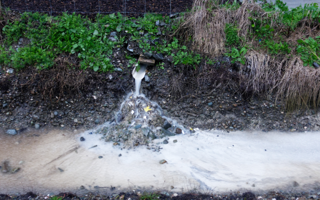 A white drain pipe emptying water into a stream.