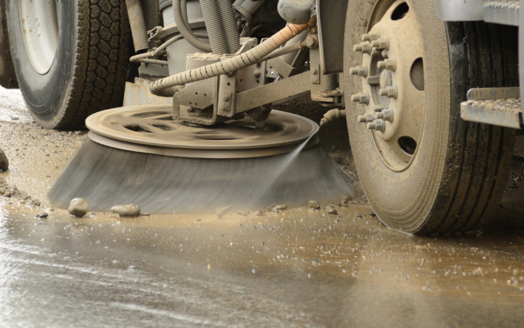 Sweeper truck sweeping up gravel and mud from a paved surface,