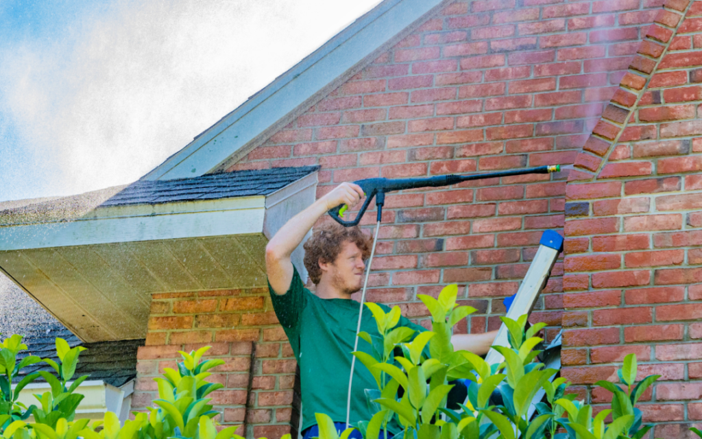 Man pressure washing the exterior of a red brick house.